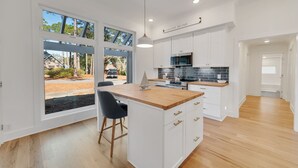 Een moderne keuken met witte kastjes, een houten eiland en grote ramen met uitzicht op de omgeving.