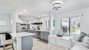 A modern kitchen with a central island, grey cabinets, and a dining area with a white table and bench.