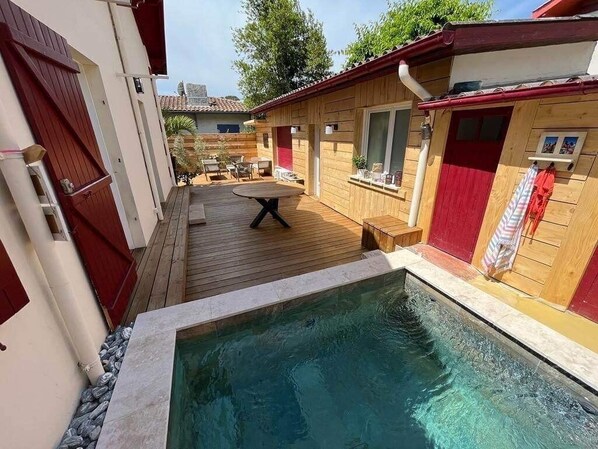 A pool area with a wooden deck, a small table, and a red door. - A charming Arcachonnaise home with all the comforts (ARCACHON)