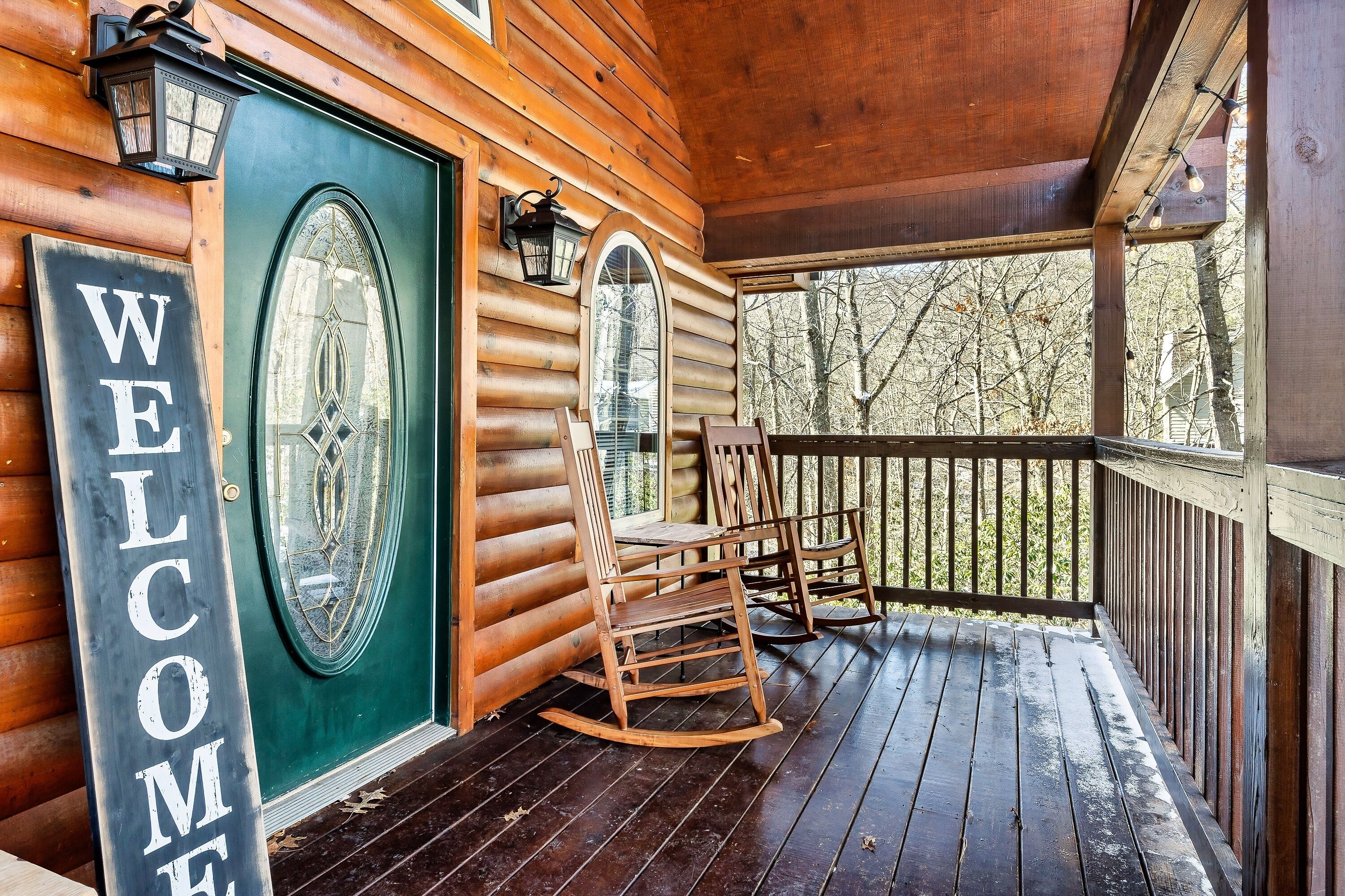 A wooden cabin with a green door, a welcome sign, and a porch with rocking chairs.