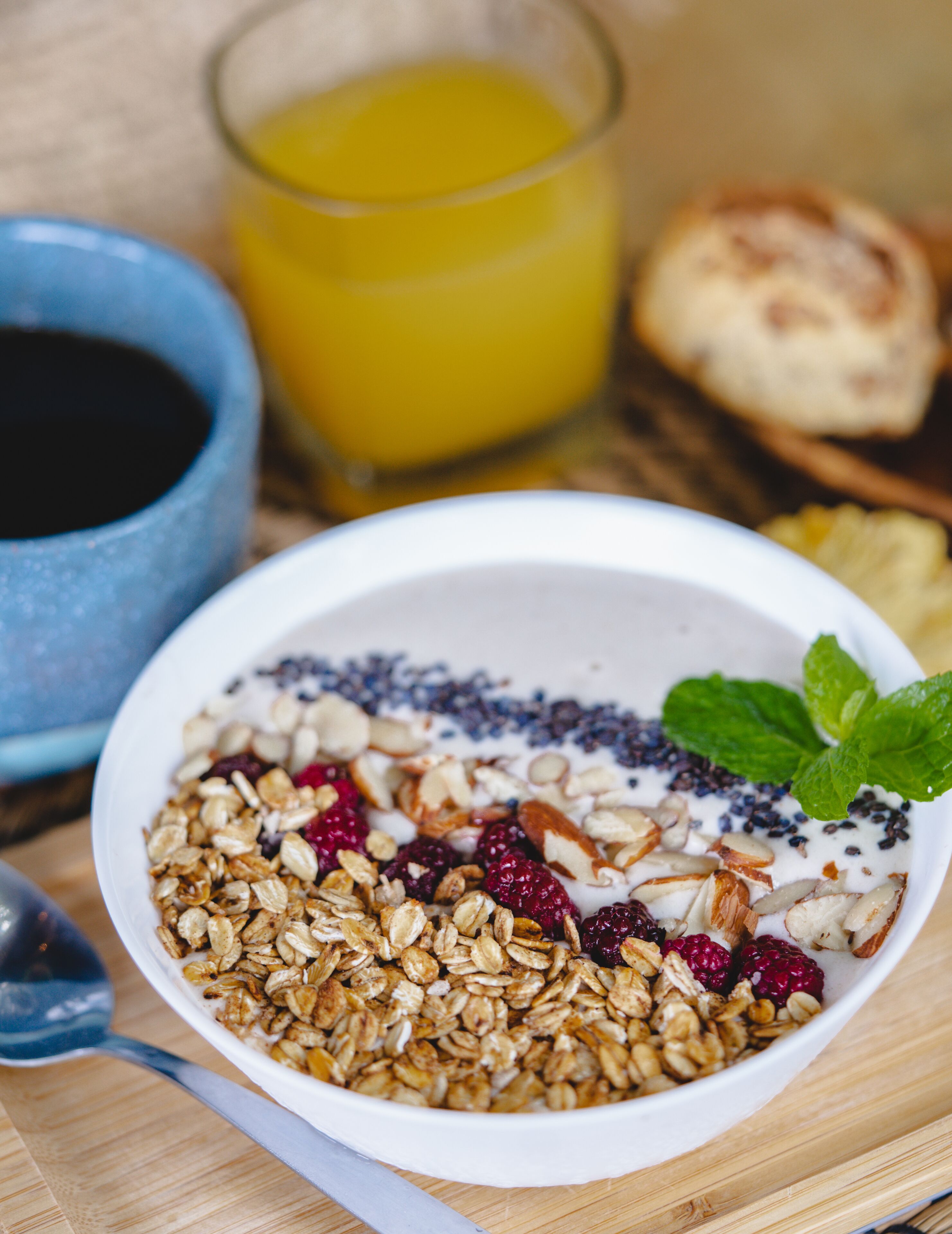 A bowl of granola with fruits and nuts, a glass of orange juice, and a cup of coffee on a wooden table.