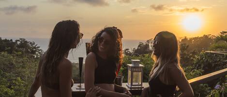 Three people standing on a wooden deck overlooking a body of water during sunset.