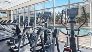 A gym with treadmills, ellipticals, and a pool visible through large windows. - Lazy River and Indoor Pool Sleeps 8 CT605 (Gulf Shores)