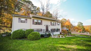 Traditional home with a central entrance and front porch, set amidst a well-manicured yard with a small garden and mature trees.
