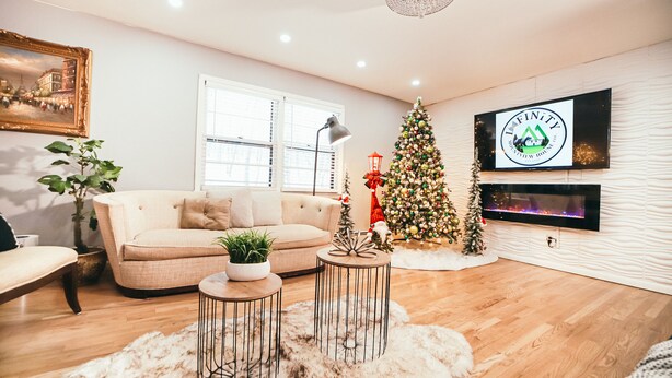Un soggiorno accogliente con un divano beige, un albero di Natale, un televisore a schermo piatto e un lampadario.