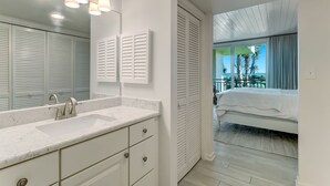 Un baño moderno con lavamanos de mármol, un espejo grande y un vestidor con contraventanas blancas.