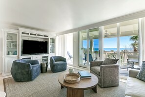A modern living room with a flat-screen TV, comfortable seating, and a view of the ocean.