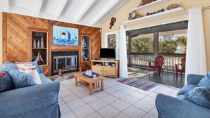 A living room with a fireplace, a television, and a balcony with red chairs. - Doubloon: Beach, Private Pool and Boating....This 4 Bedroom home has it all!! (Placida)