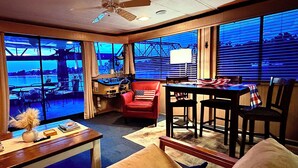 Ein Zimmer mit Blick auf eine Brücke, ein roter Sessel, ein Tisch mit einer amerikanischen Flagge und ein Deckenventilator.
