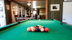 A pool table with balls in the center of a room with wooden walls and a door on the right. - Historic Date Creek Ranch (Congress)
