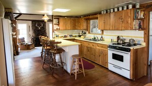 A kitchen with wooden cabinets, a central island with stools, a stove, and a sink. - Historic Date Creek Ranch (Congress)