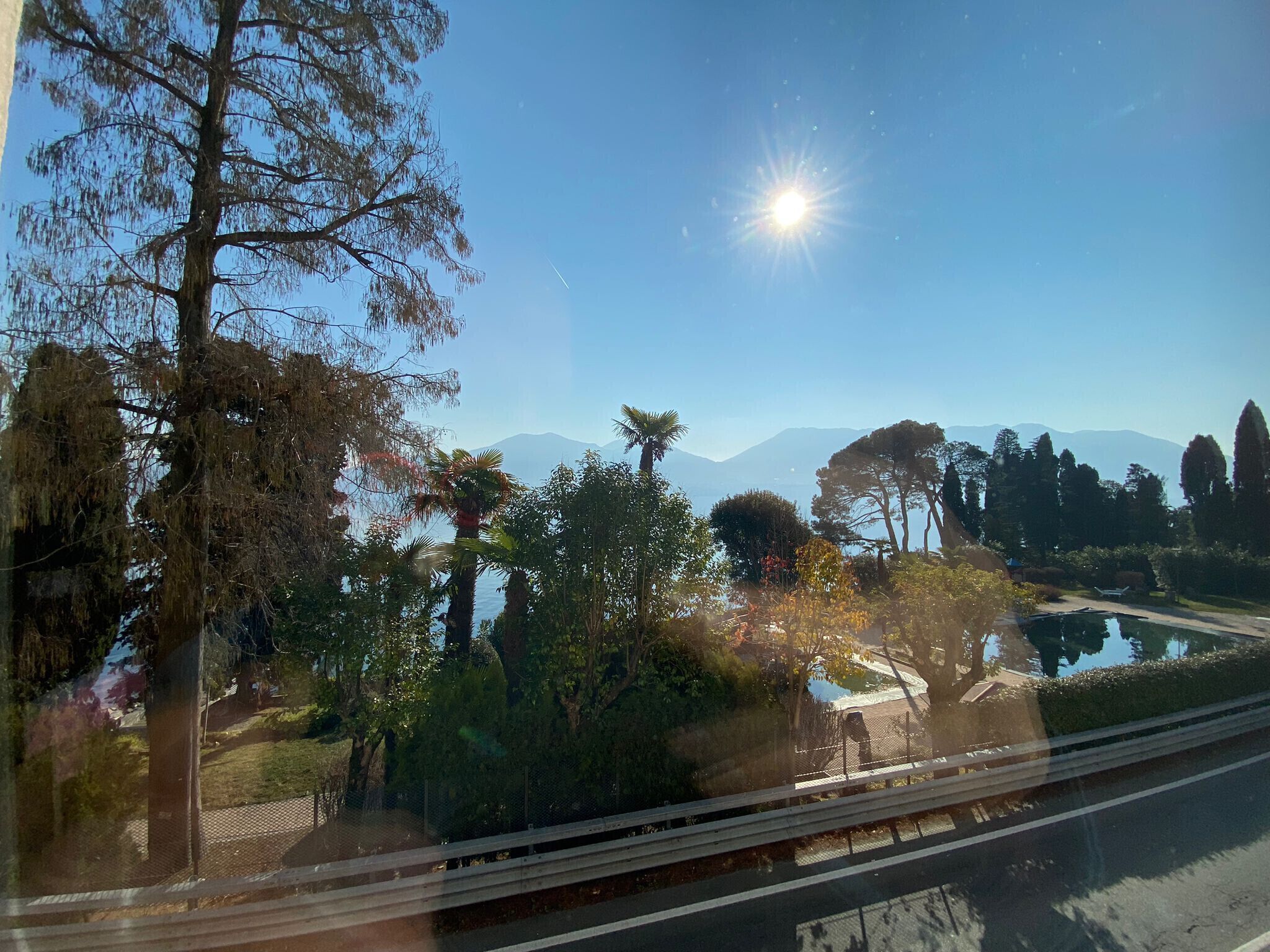 Une vue depuis une fenêtre donnant sur un espace paysager agrémenté d’arbres et d’un plan d’eau, avec des montagnes en arrière-plan.