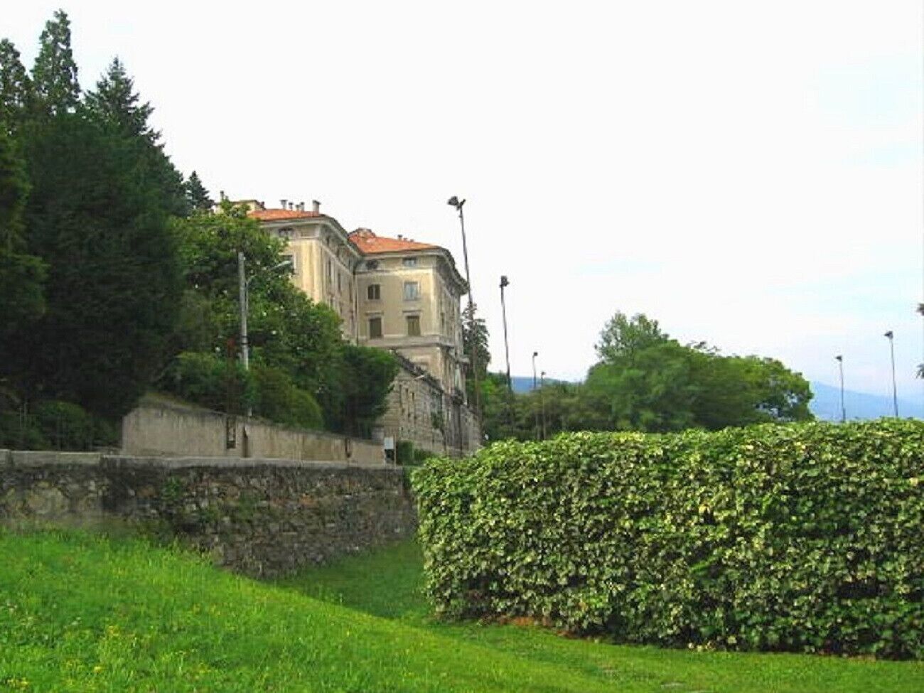 Un bâtiment historique doté d’un mur en pierre et d’une haie bien entretenue en premier plan.