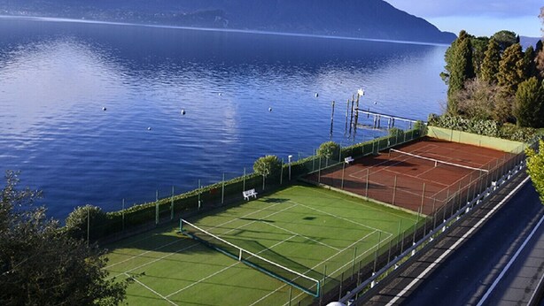 Tenniskenttä sijaitsee järven vieressä, ja taustalla näkyy vuoristo.