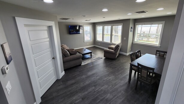 A spacious living room with a dark wood floor, a gray sofa, a coffee table, and a TV mounted on the wall. - Paradise on Lake Harris Apt #202 (Leesburg)