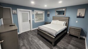 A bedroom with a bed, bedside tables, a dresser, a door, and a window with blinds. - Paradise on Lake Harris Apt #202 (Leesburg)