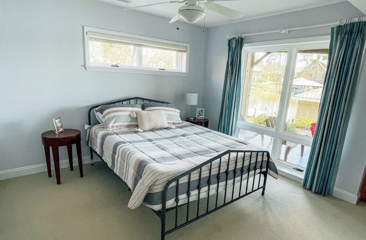 Ein Schlafzimmer mit einem Bett, einem Nachttisch, einem Fenster mit Vorhängen und einem Deckenventilator.