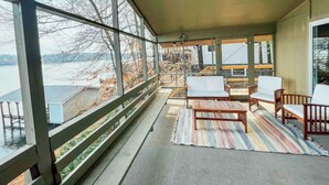 Un espace extérieur abrité, avec vue sur un plan d’eau, doté de mobilier en bois et d’un tapis à rayures.