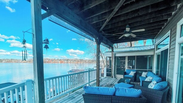 Une terrasse extérieure couverte, aménagée avec des meubles en osier et offrant une vue sur un lac.