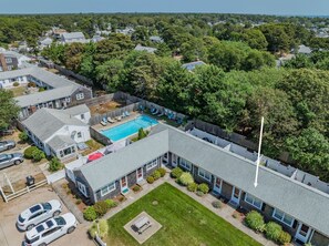 A residential area with a swimming pool surrounded by a fence, houses, and trees. - Cozy Mid-Cape Studio Steps to the Beach & Pool (Dennis Port)
