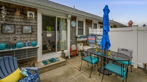 A patio with outdoor furniture, a blue umbrella, and decorative items on the wall. - Cozy Mid-Cape Studio Steps to the Beach & Pool (Dennis Port)