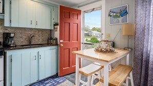 A kitchen with light blue cabinets, a red door, and a wooden table with a bench. - Charming Dennis Port Getaway for Two with Pool & Walk to Beach (Dennis Port)