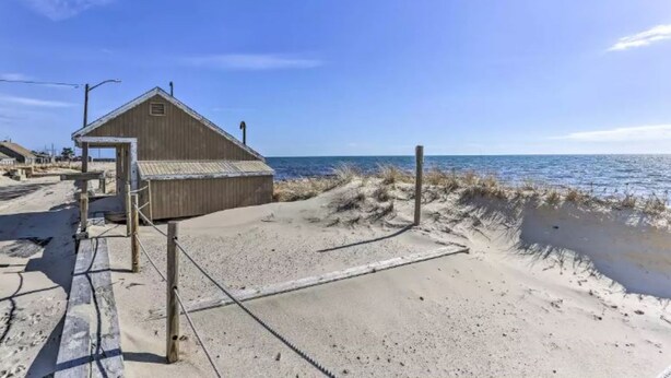 A beach house with a wooden exterior, a concrete deck, and a view of the ocean. - Charming Dennis Port Getaway for Two with Pool & Walk to Beach (Dennis Port)