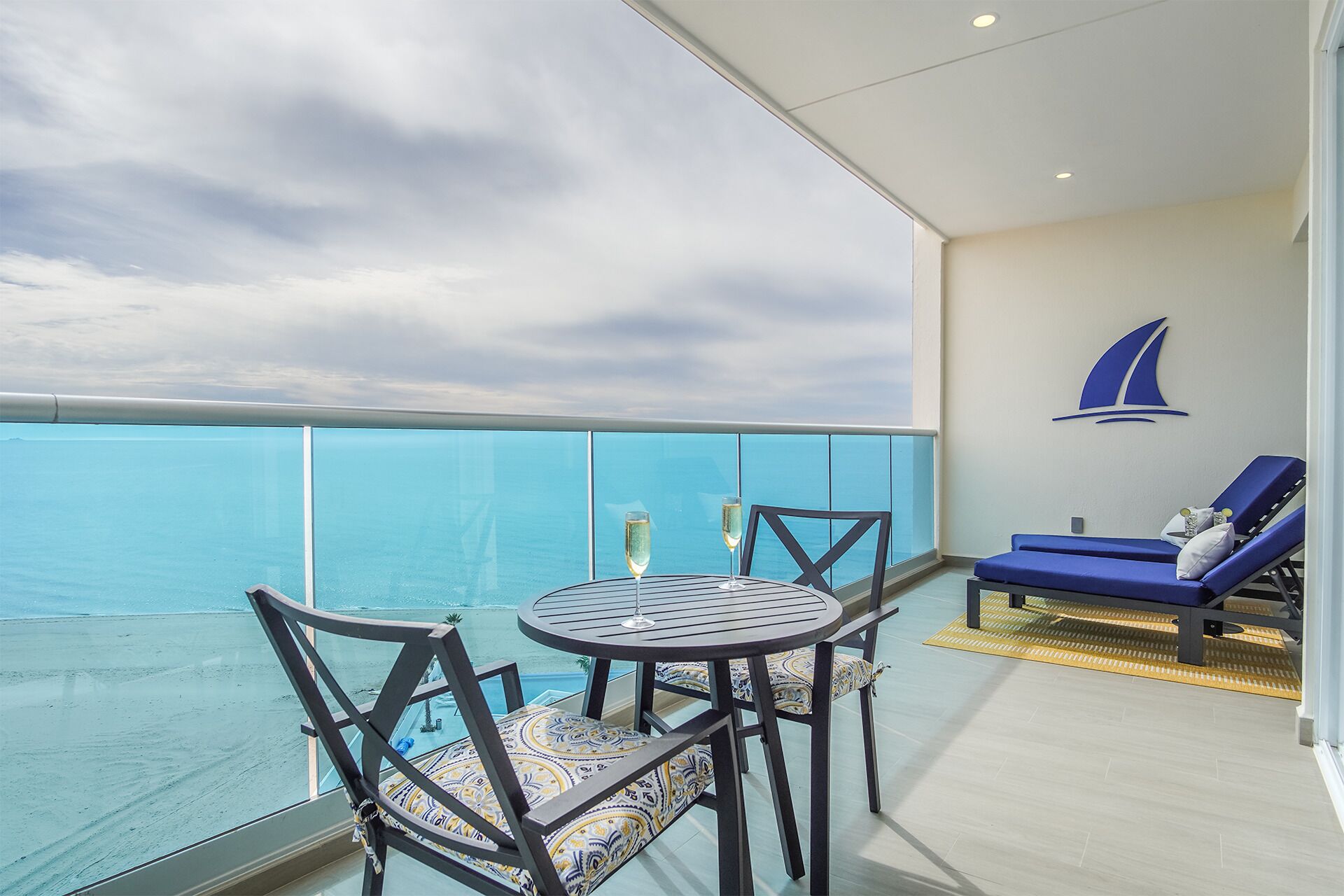 Un balcon avec une table et des chaises, un fauteuil de relaxation et une décoration murale représentant un voilier.