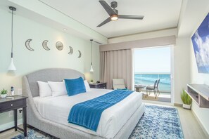 Ein modernes Hotelzimmer mit einem großen Bett, einem Deckenventilator, einem Balkon mit Meerblick und einem Schreibtisch mit Lampe.