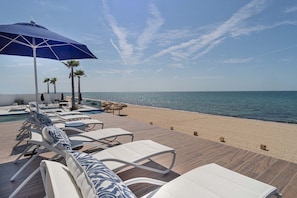 A beachside lounge area with sun loungers, a pool, and a view of the sea.