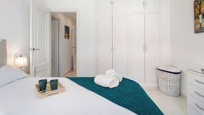 Una habitación de hotel con una cama, una mesita de noche con lámpara, un armario grande y un cuadro en la pared.