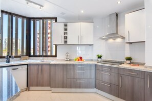 A modern kitchen with a granite countertop, white cabinets, and a stainless steel range hood.