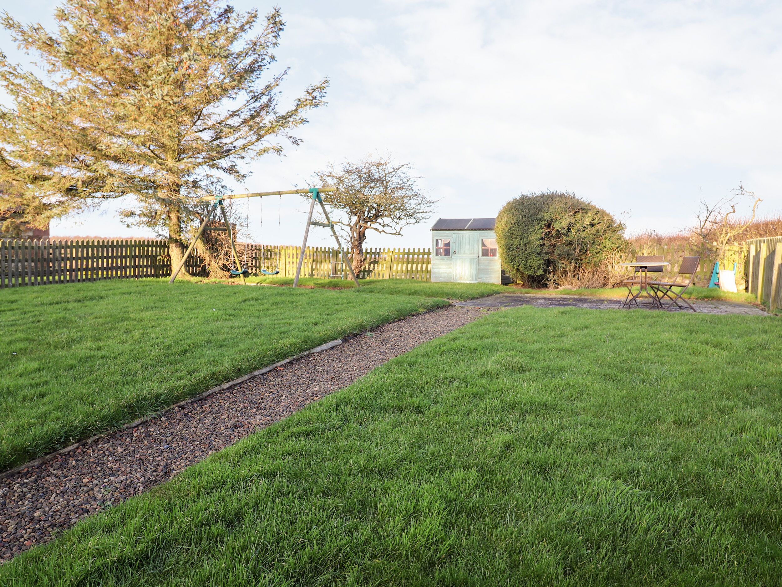 Ein Garten mit Rasen, einer Schaukel, einem kleinen Gartenhaus und einer Hecke.
