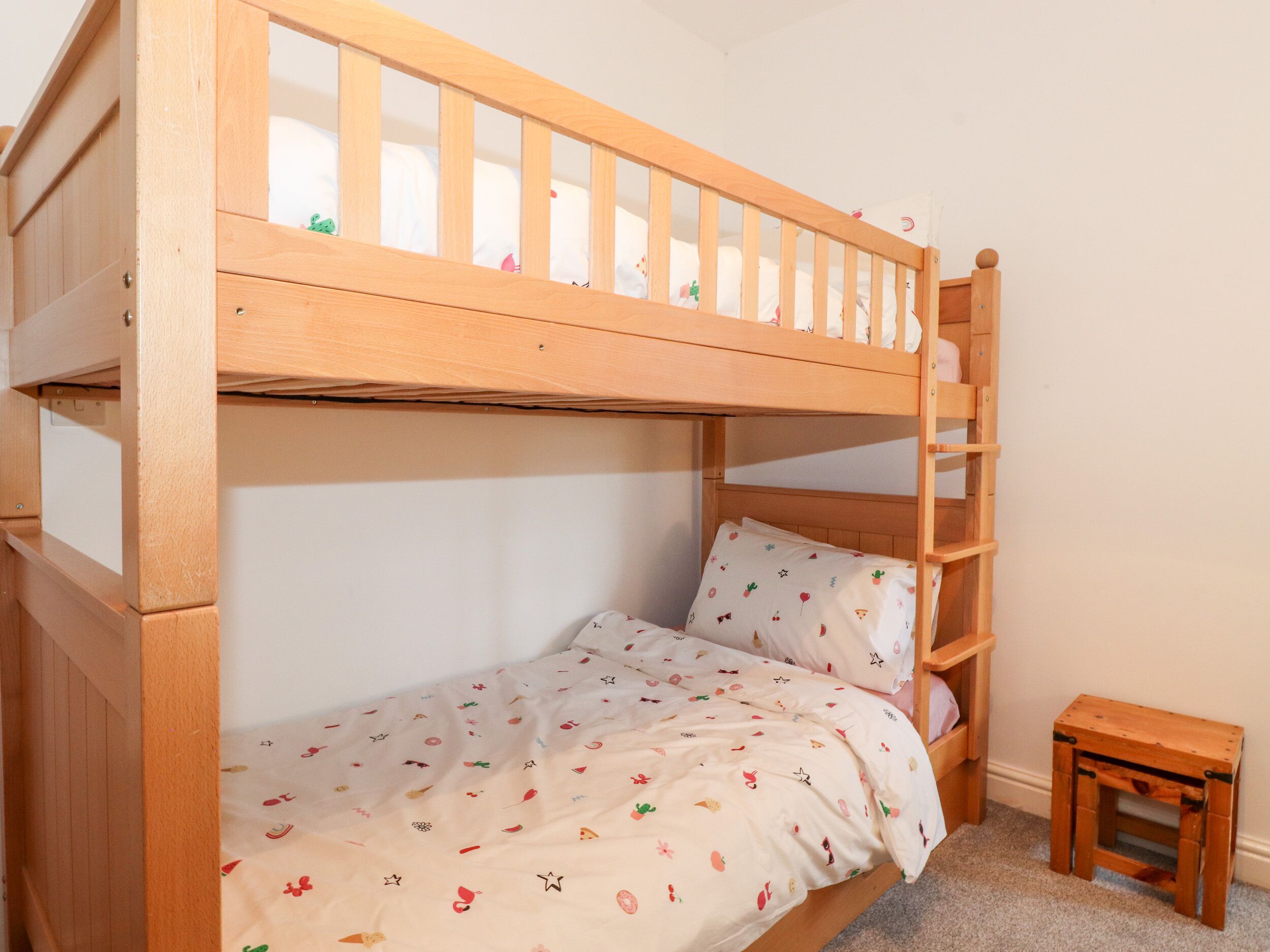 A bunk bed with a wooden frame, a small wooden stool, and a patterned bedspread.