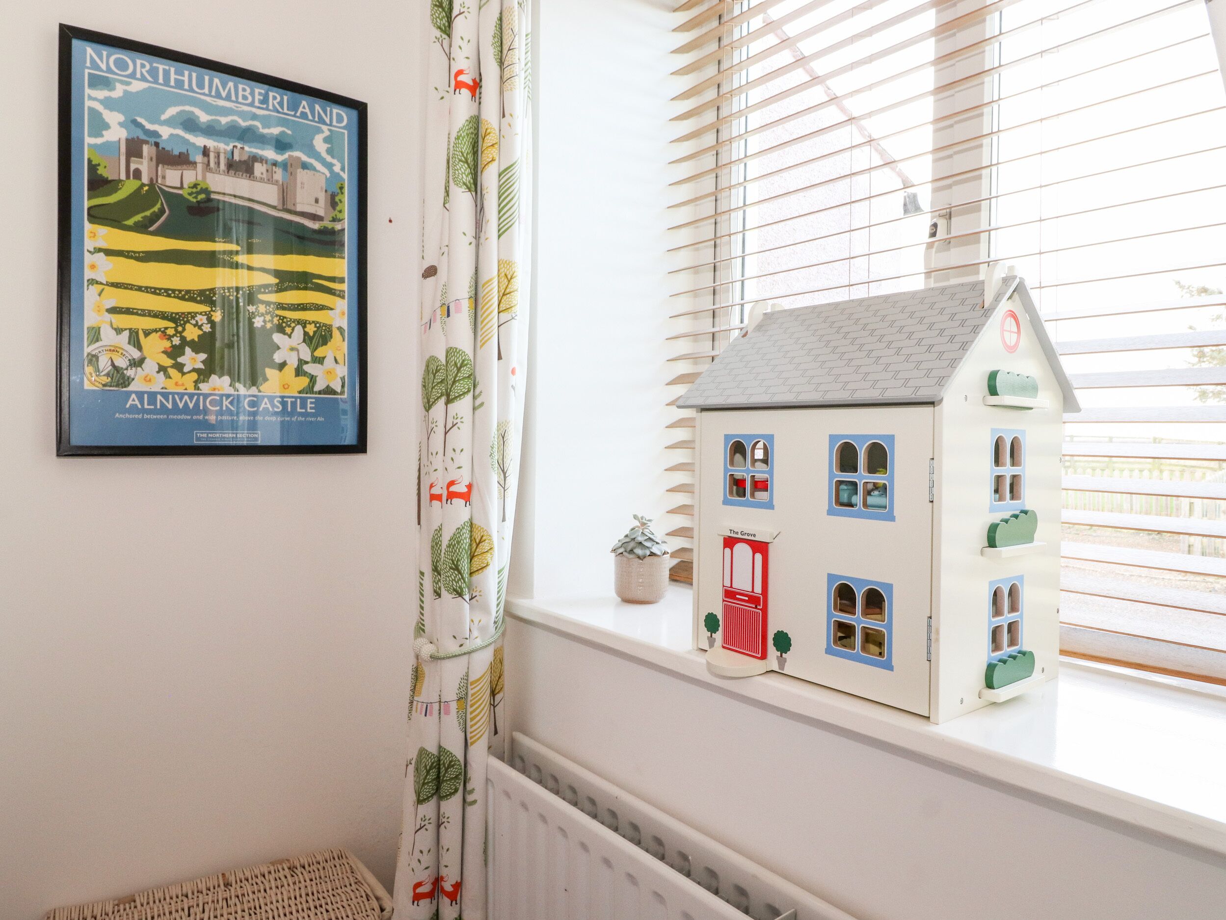 A room with a framed poster of Northumberland Land, a small house model on a windowsill, and a curtain with a nature pattern.