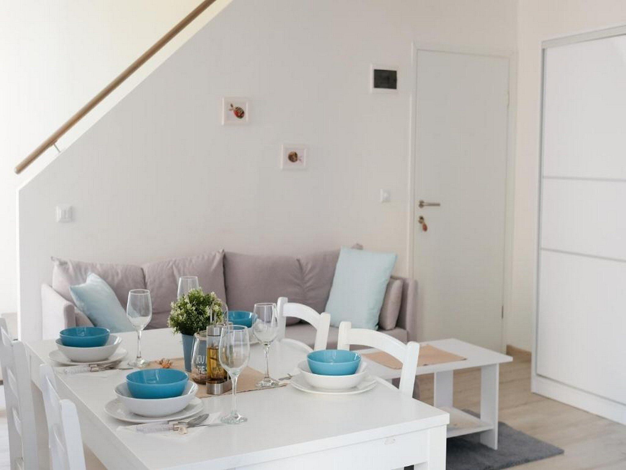 A dining area with a white table set for four, blue and white plates, and glasses. There is a white chair and a sofa with cushions in the background.