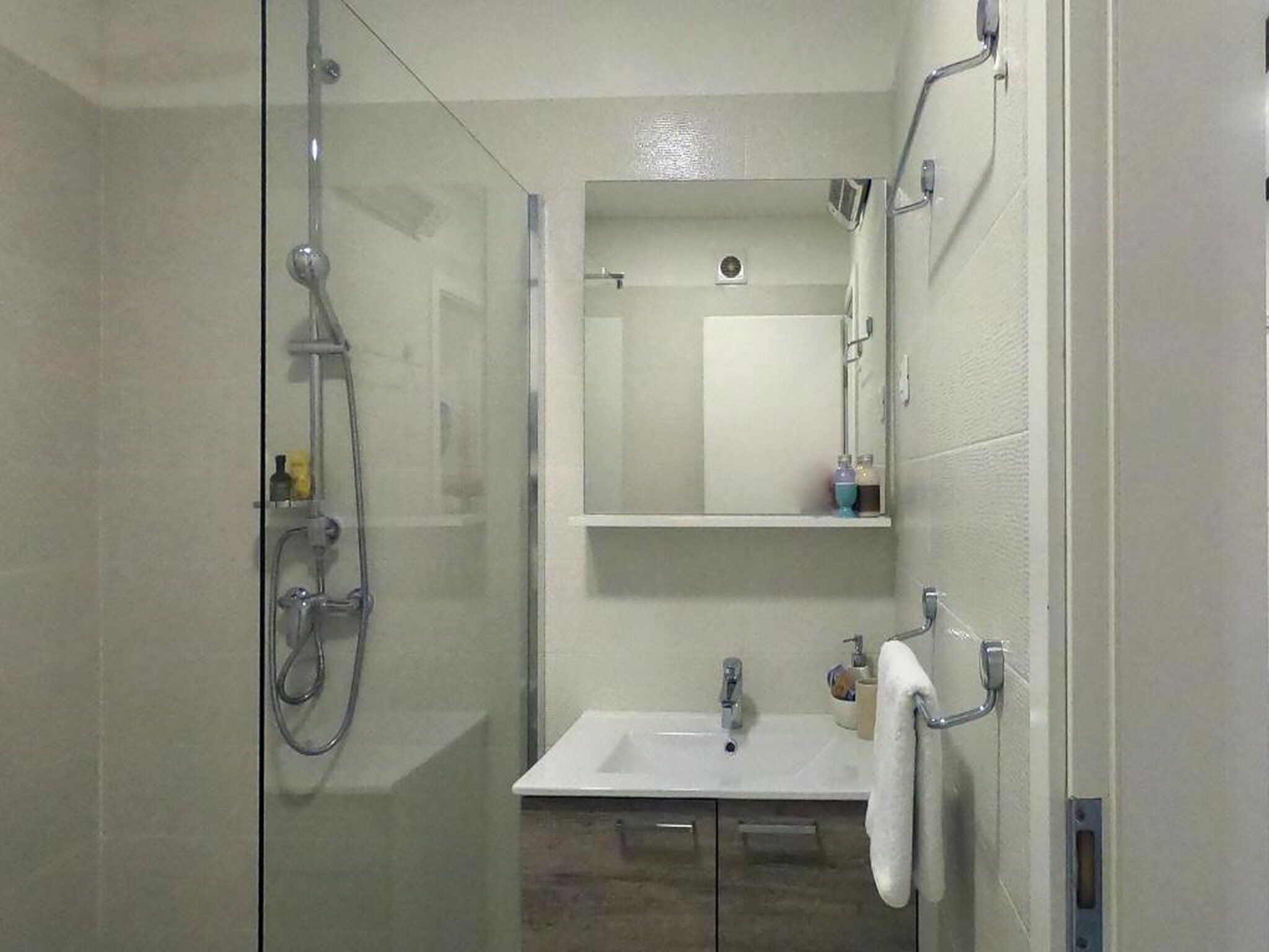 Un baño con cabina de ducha de vidrio, un lavabo blanco y un espejo sobre él.