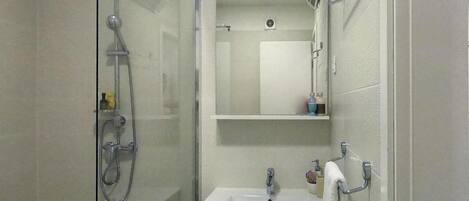 Un baño con cabina de ducha de vidrio, un lavabo blanco y un espejo sobre él.