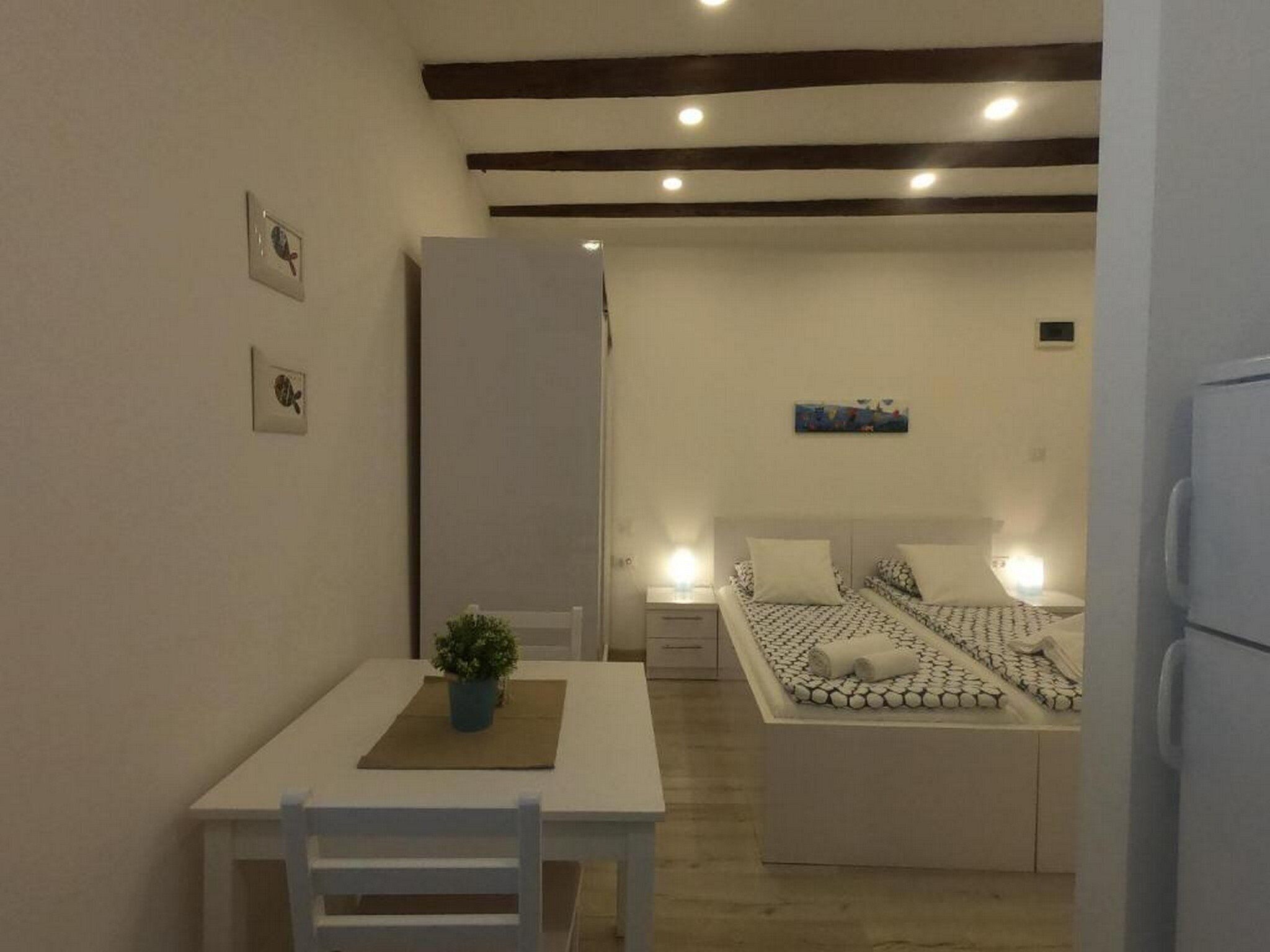 Habitació petita i ben il·luminada amb un llit, una taula i una cadira, i una petita planta.
