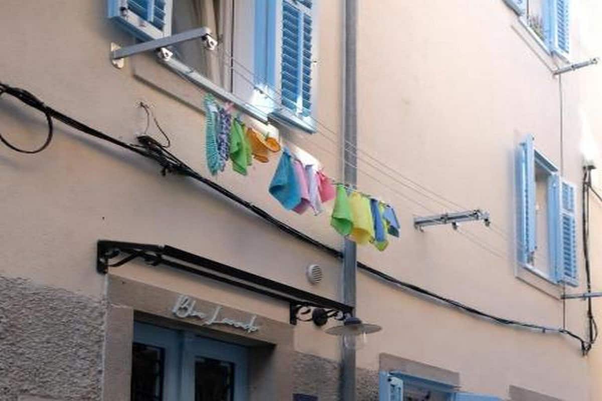 A building with a blue door, a small outdoor seating area with white chairs, and a row of colorful umbrellas hanging above the entrance.