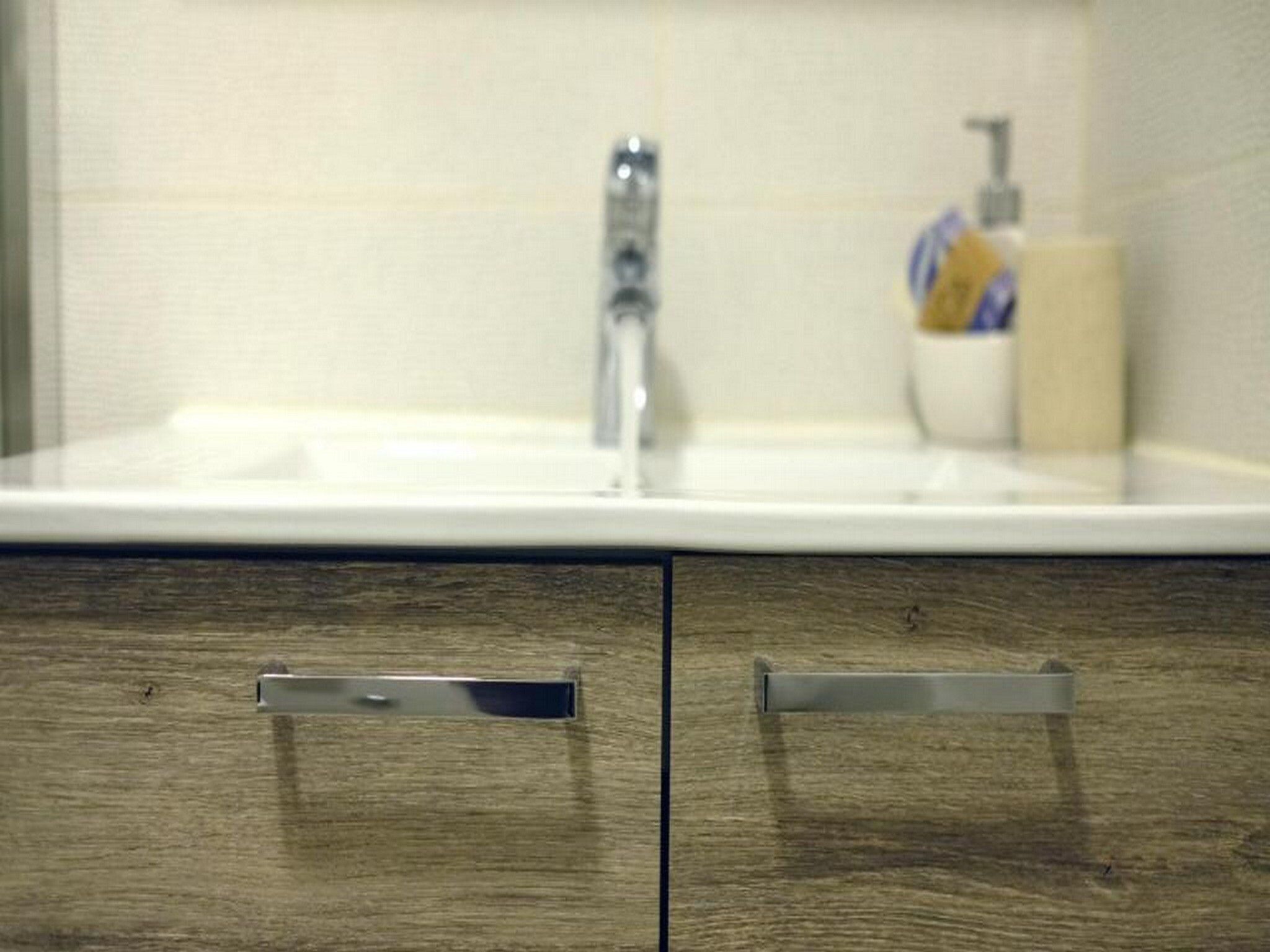 A bathroom with a wooden vanity, a white sink, and a soap dispenser.