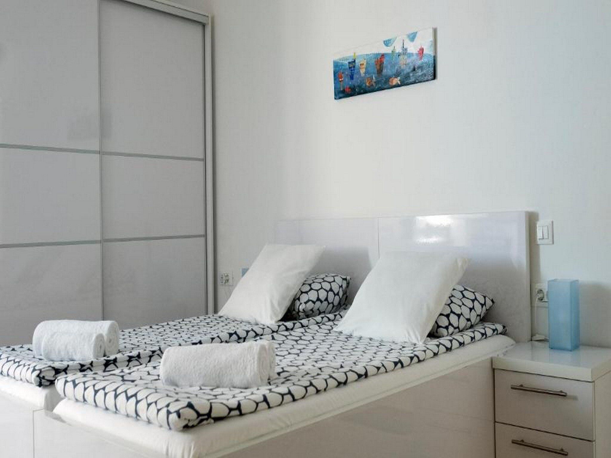 A neatly made bed with a patterned bedspread, two pillows, and two rolled towels.