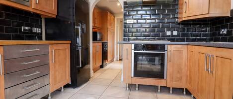 A modern kitchen with wooden cabinets, a black refrigerator, a glass-top island, and a tiled backsplash.