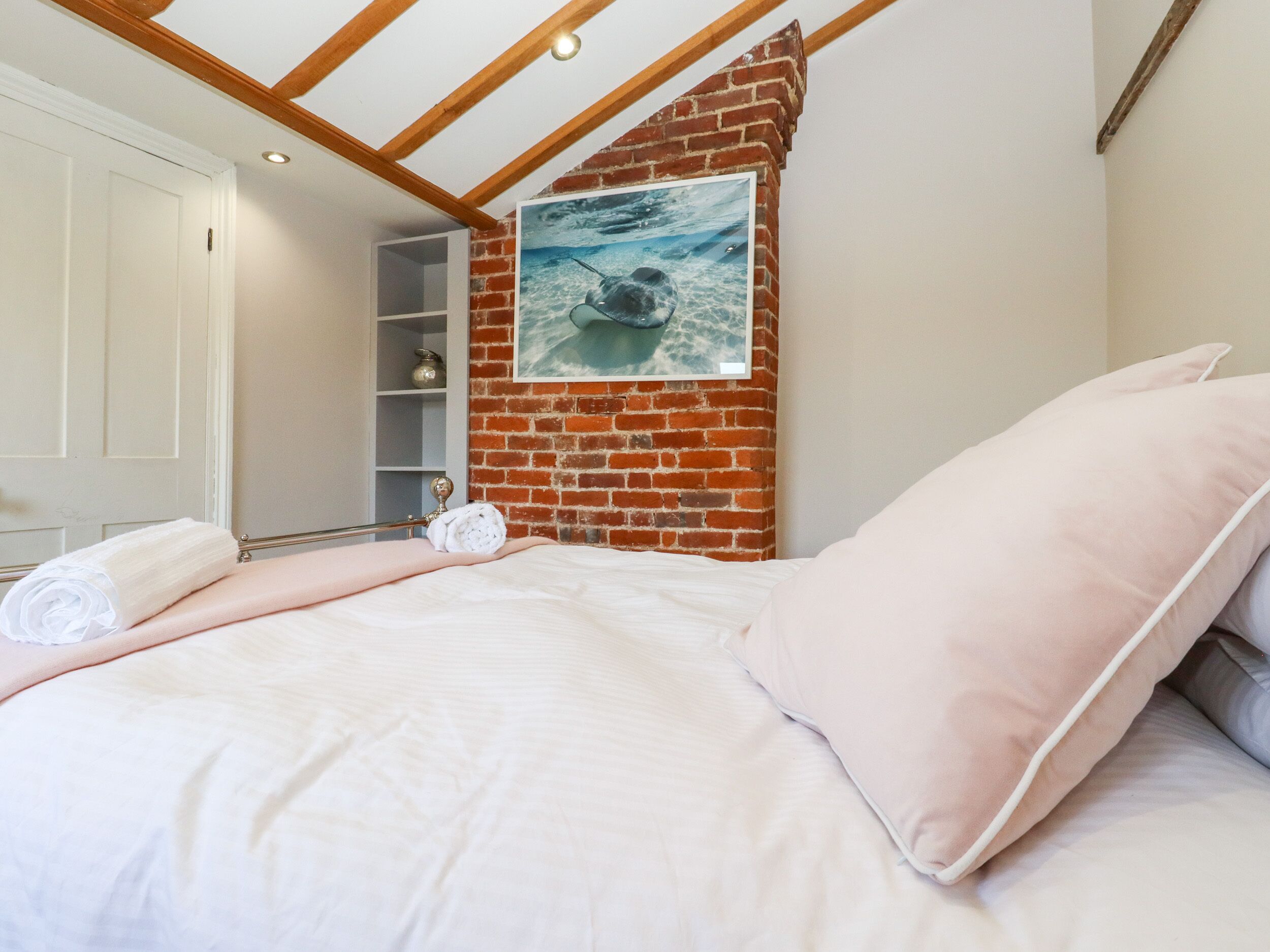 A bedroom with a brick wall, a bed with white bedding, a shelf unit, and a framed picture of an underwater scene.