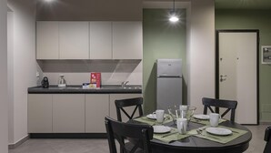 A compact kitchen with a dining area, featuring a refrigerator, sink, and a table set for four. - San Luca Apartments - Grillo by Wonderful Italy (Genoa)