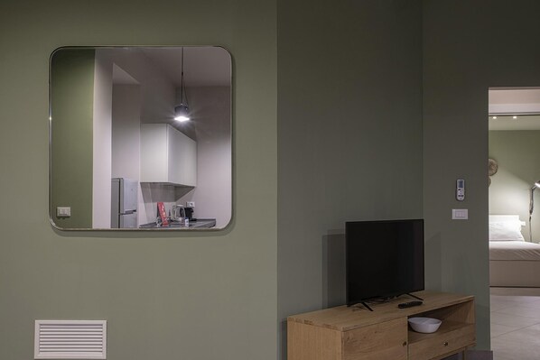 A modern room with a large mirror, a flat-screen TV, a wooden cabinet, and a bed in the background.