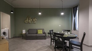 A living room with a gray sofa, a dining table with chairs, a washing machine, and pendant lights. - San Luca Apartments - Grillo by Wonderful Italy (Genoa)
