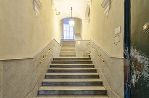 A marble staircase with handrails, leading to a bright room with a chandelier.
