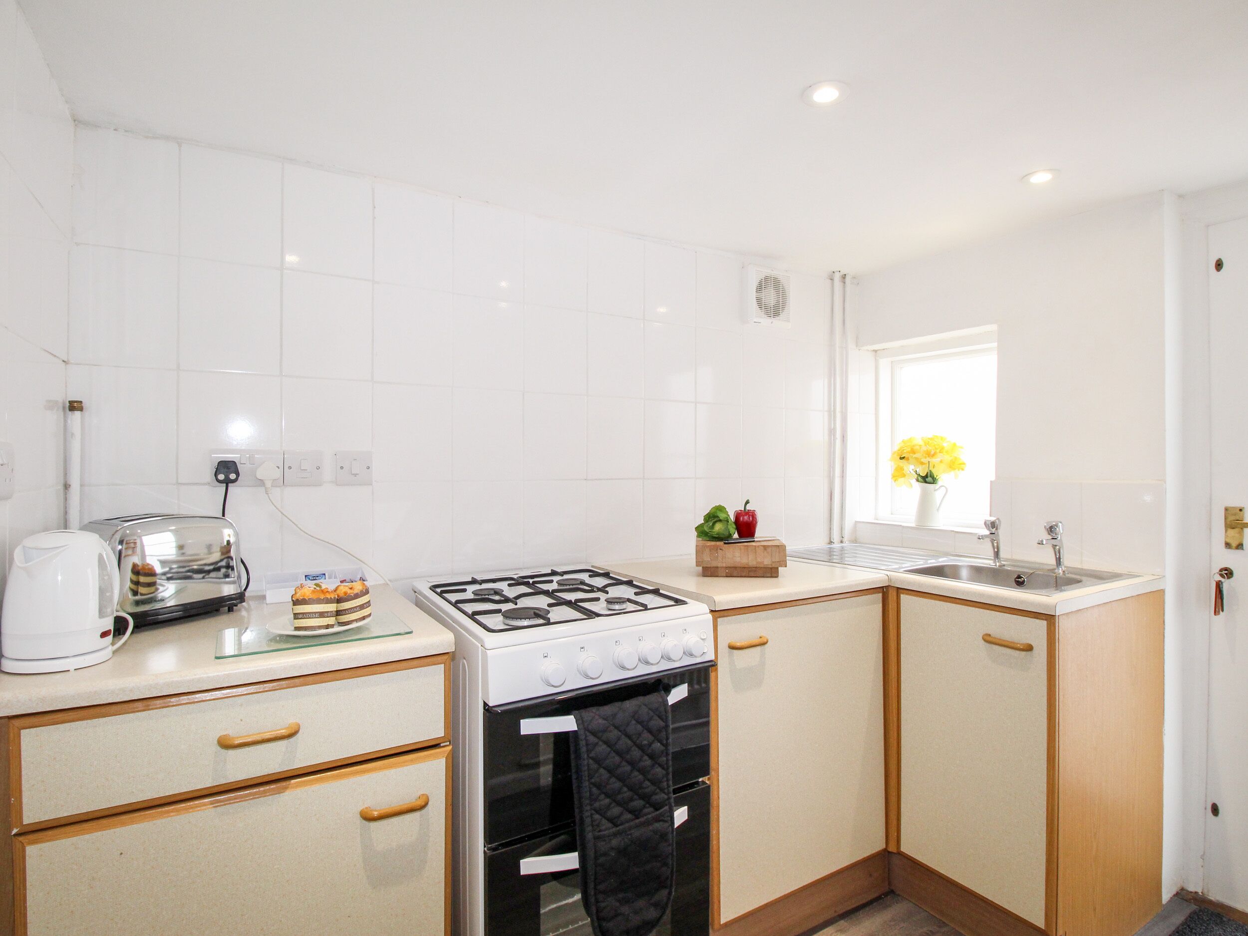 A compact kitchen with white tiles, a gas stove, a built-in oven, a toaster, and a sink.