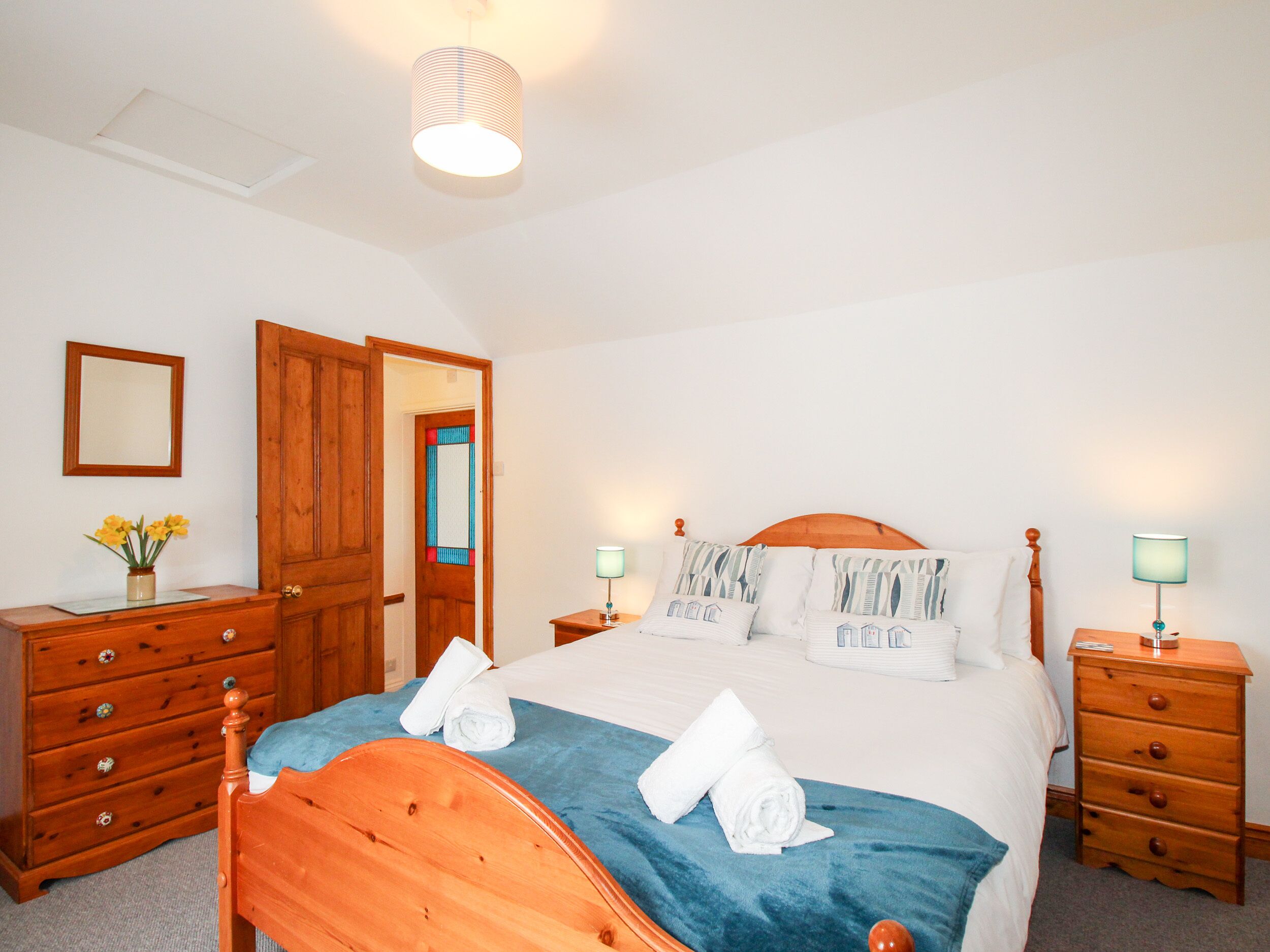 A bedroom with a wooden bed, two bedside tables with lamps, a wooden dresser, and a mirror on the wall.